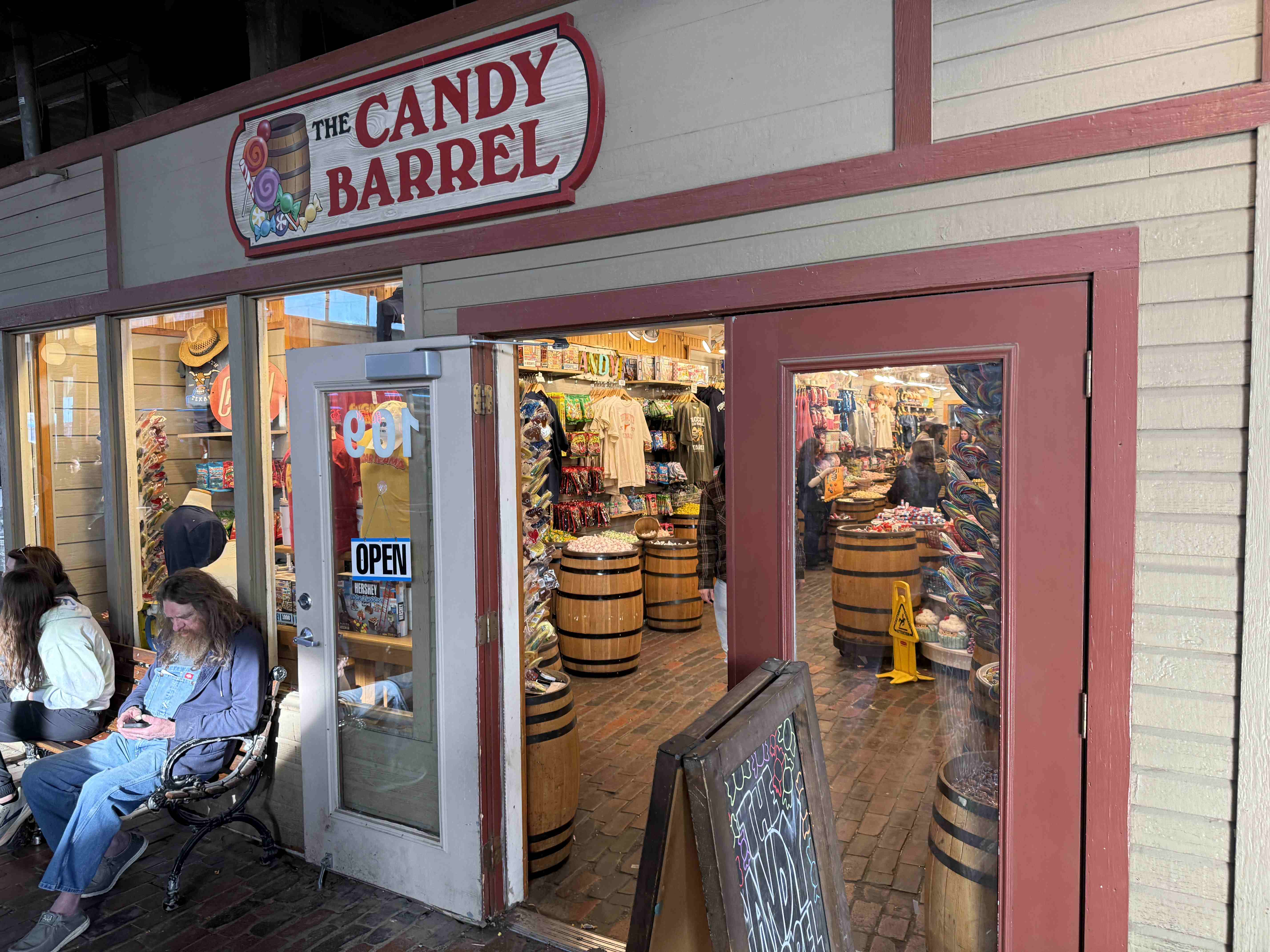 Vchod do obchodu THE CANDY BARREL s cedulí OPEN a sudy sladkostí.