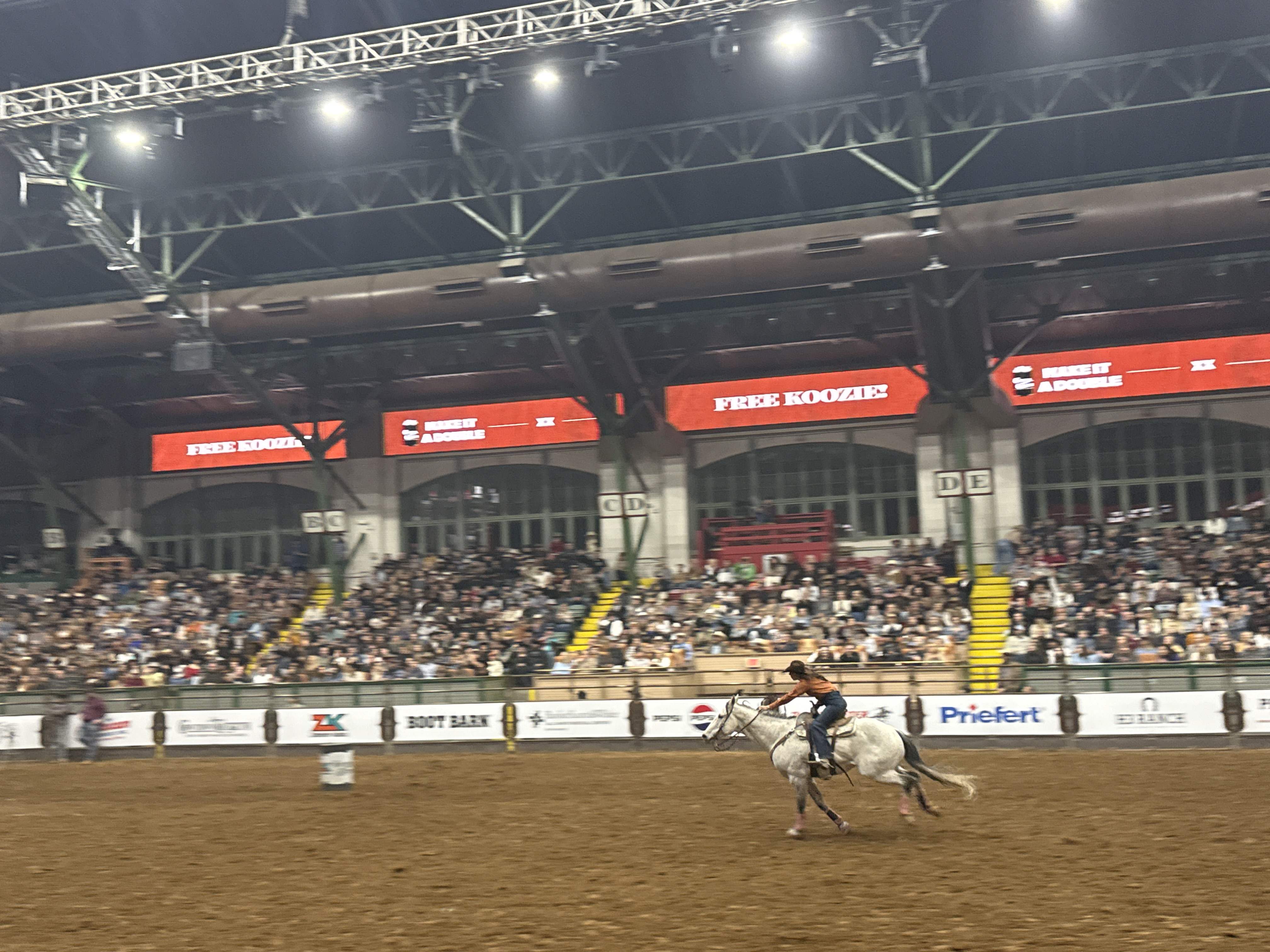 Jezdec na bílém koni v aréně, nad tribunami FREE KOOZIE, MAKE IT A DOUBLE.