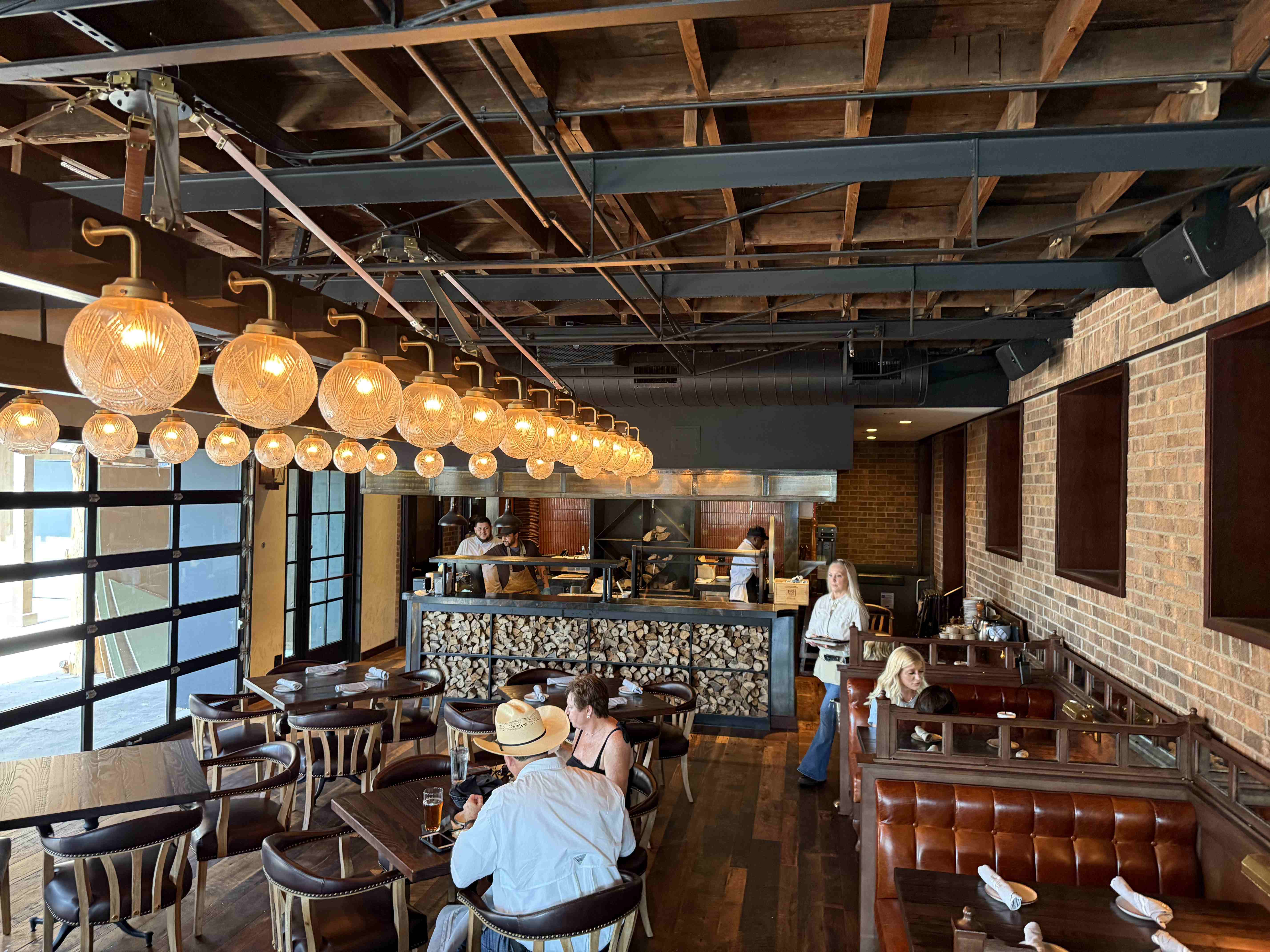 Interiér restaurace ve Stockyards: otevřená kuchyň, řada kulatých lamp, hosté v kovbojském klobouku