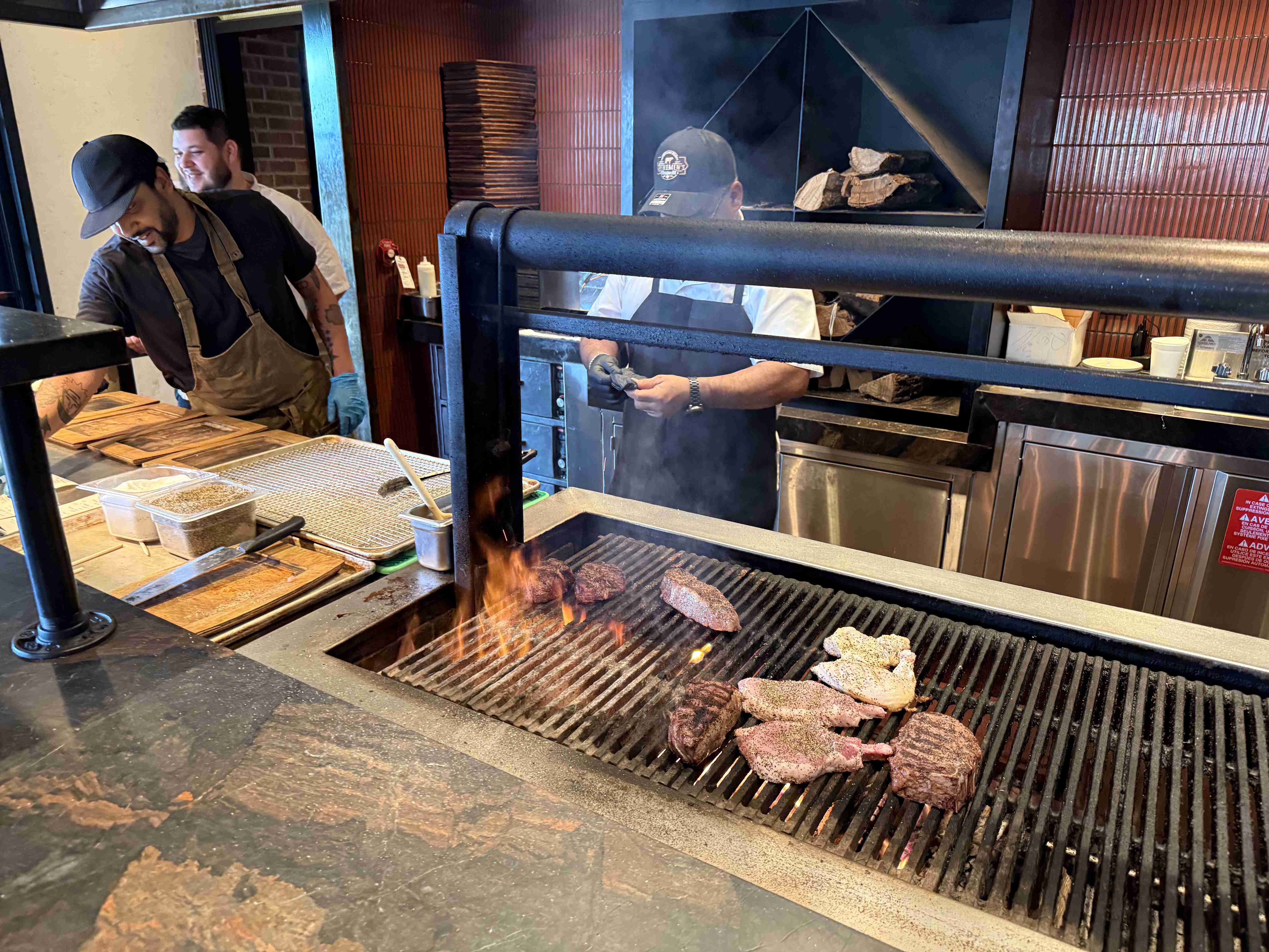 Kuchaři u otevřeného grilu, na roštu se opékají steaky a kotlety