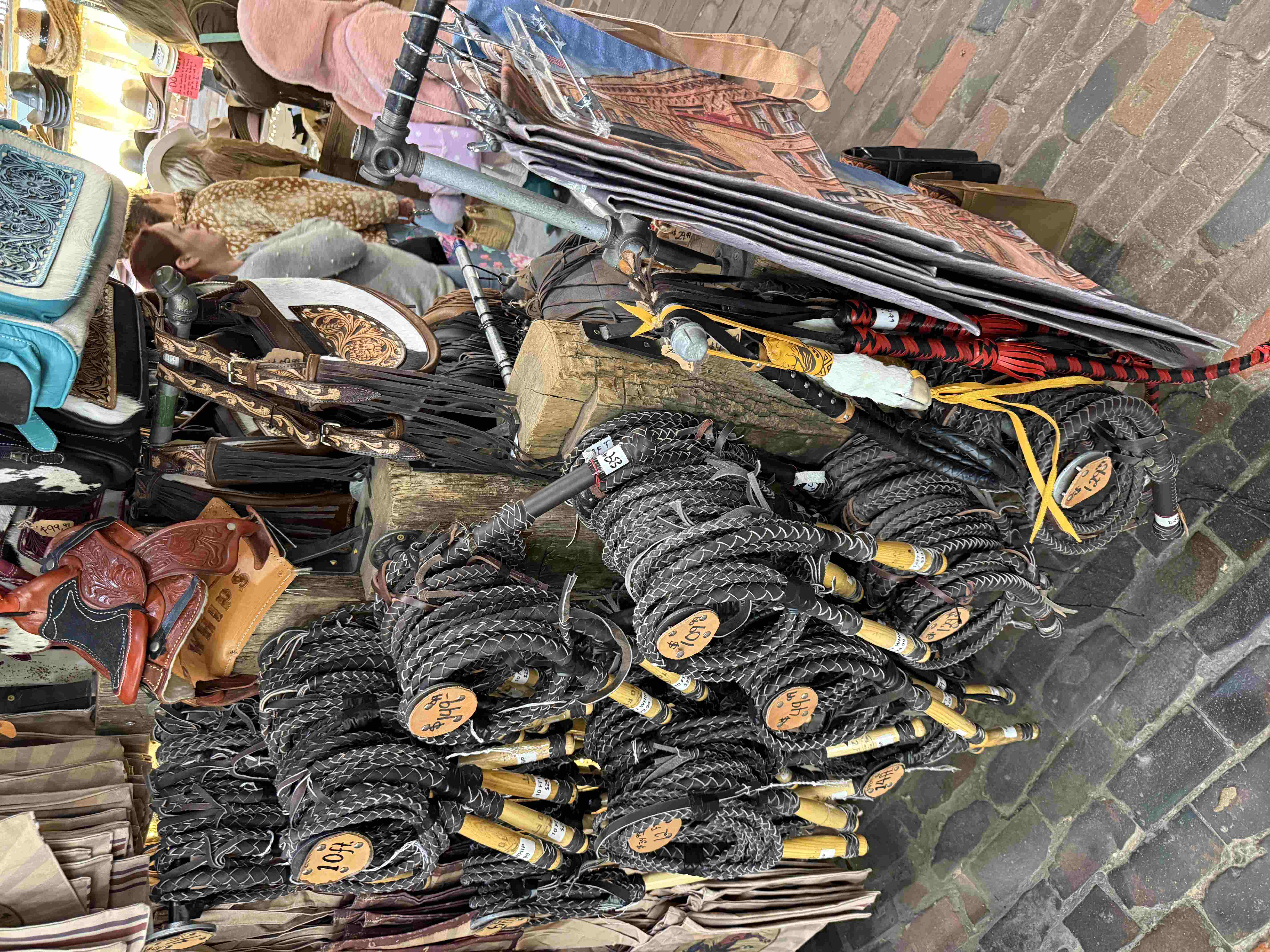Stánek s koženými biči, sedly a klobouky, cenovky 10$ a 49$