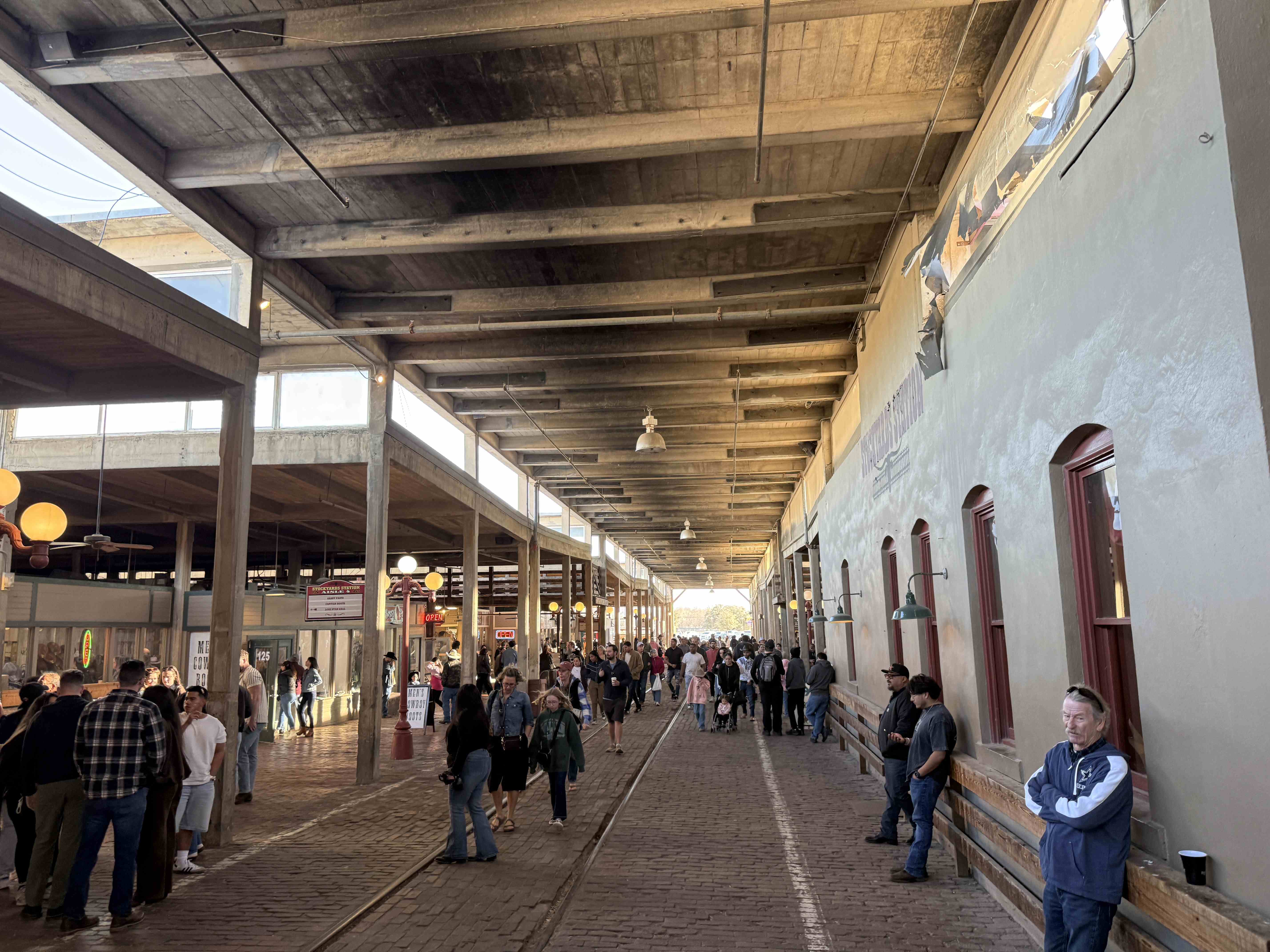 Zastřešená cihlová ulice Stockyards s davem návštěvníků a nápisy OPEN