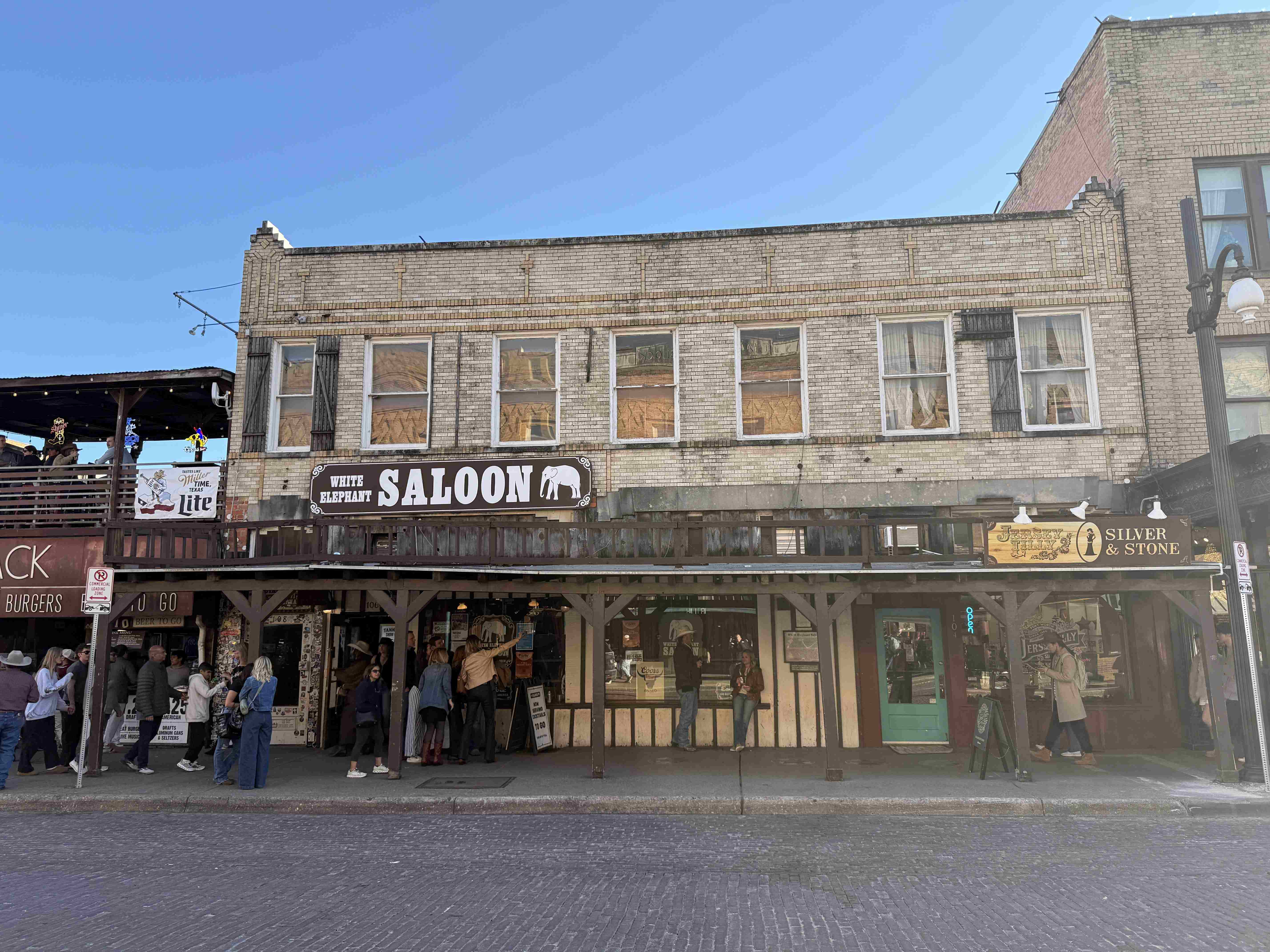 Fasáda White Elephant Saloon, nápis WHITE ELEPHANT SALOON, před vchodem postávají lidé