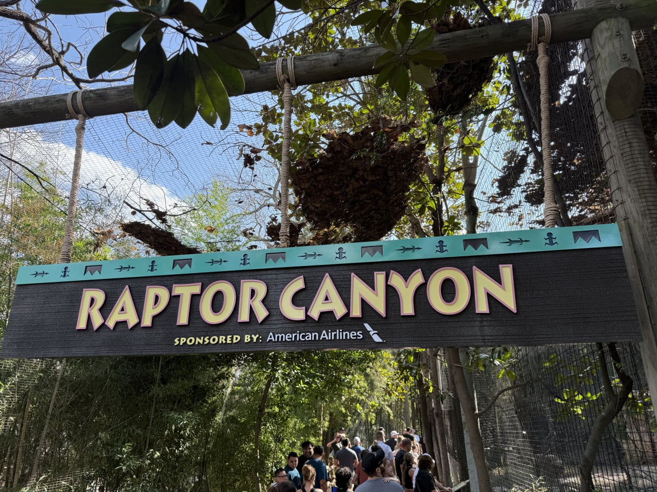 Vstupní cedule Raptor Canyon v zoo, pod ní procházejí návštěvníci.