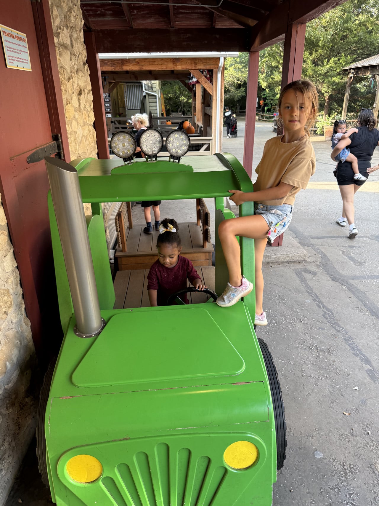 Děti si hrají na zeleném traktoru u vstupu do zoo
