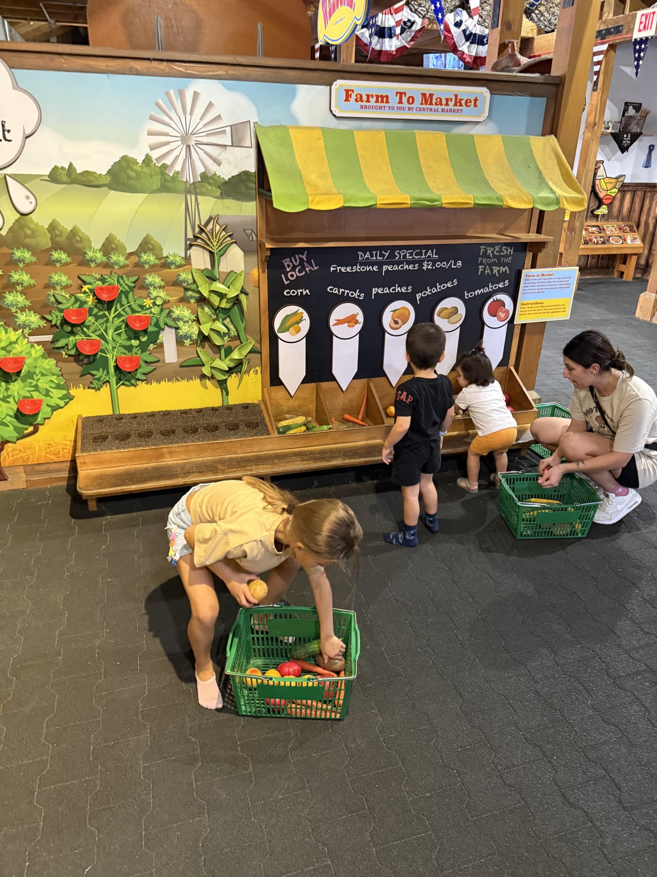 Děti si hrají na farmářském trhu s umělou zeleninou v zoo.