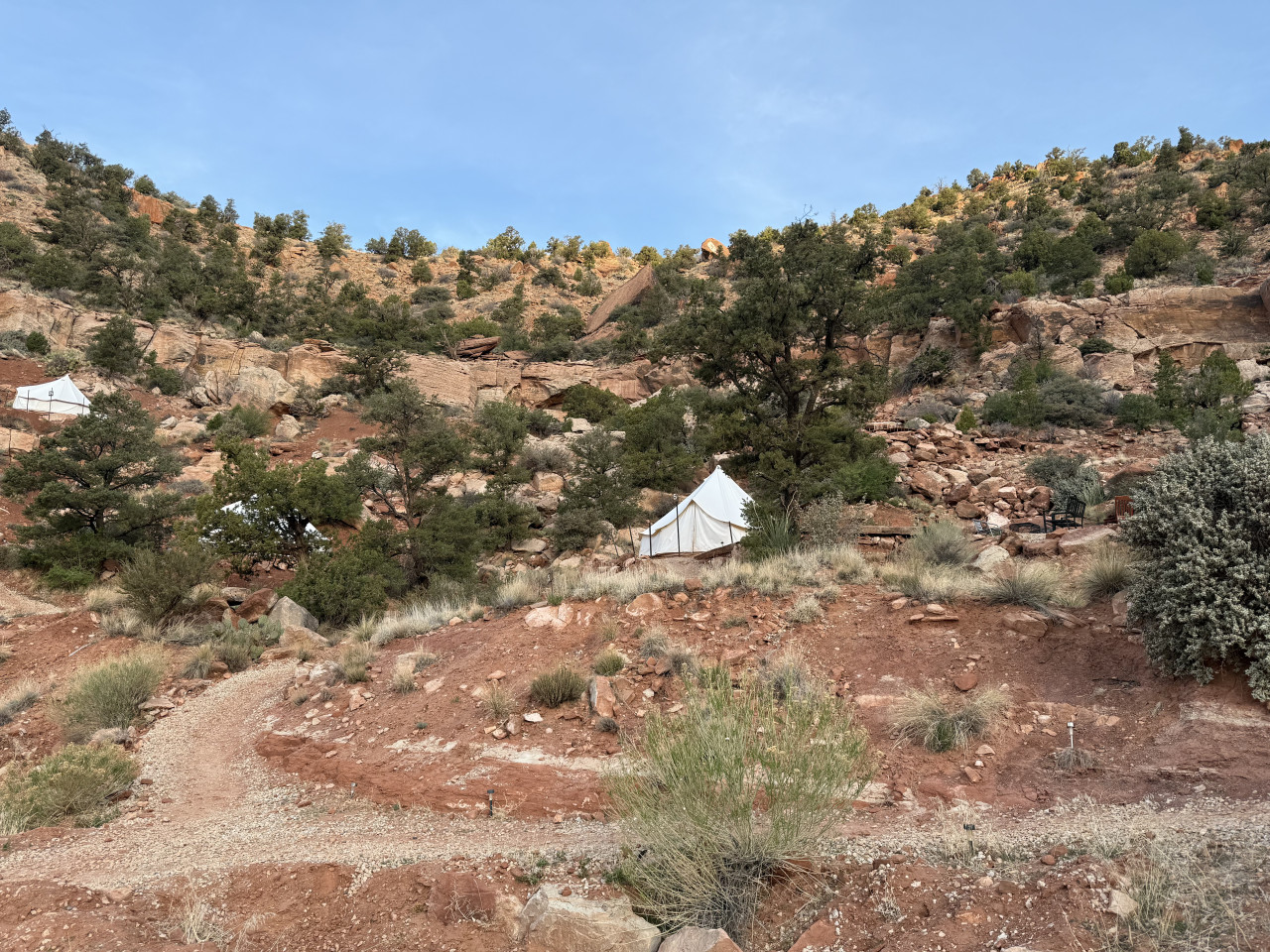 Bílé glampingové stany na kamenitém svahu kaňonu mezi keři a stromy.