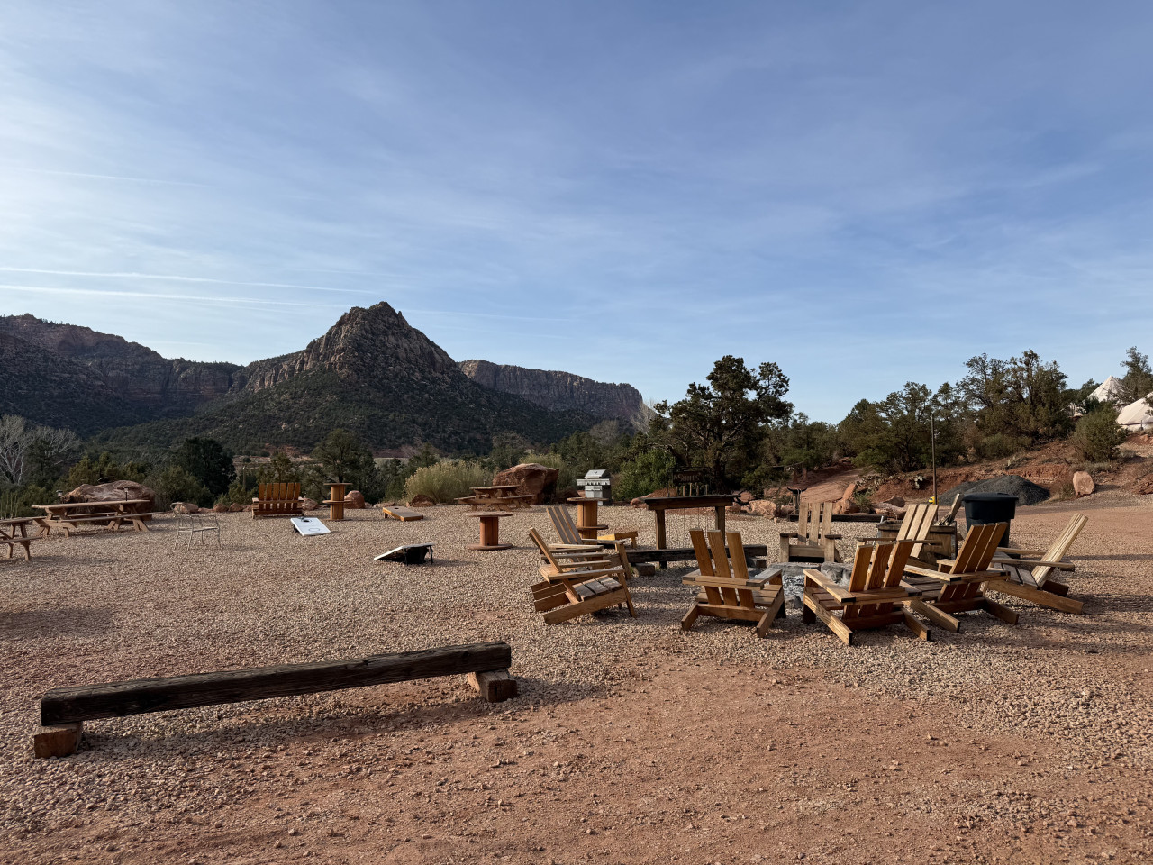 Dřevěná křesla kolem ohniště v glamping kempu, hory Zion v pozadí