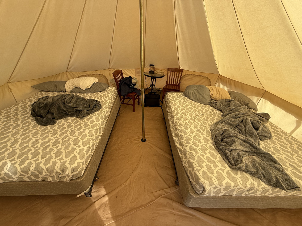 Interiér glampingového stanu: dvě postele, židle a stolek s lampou