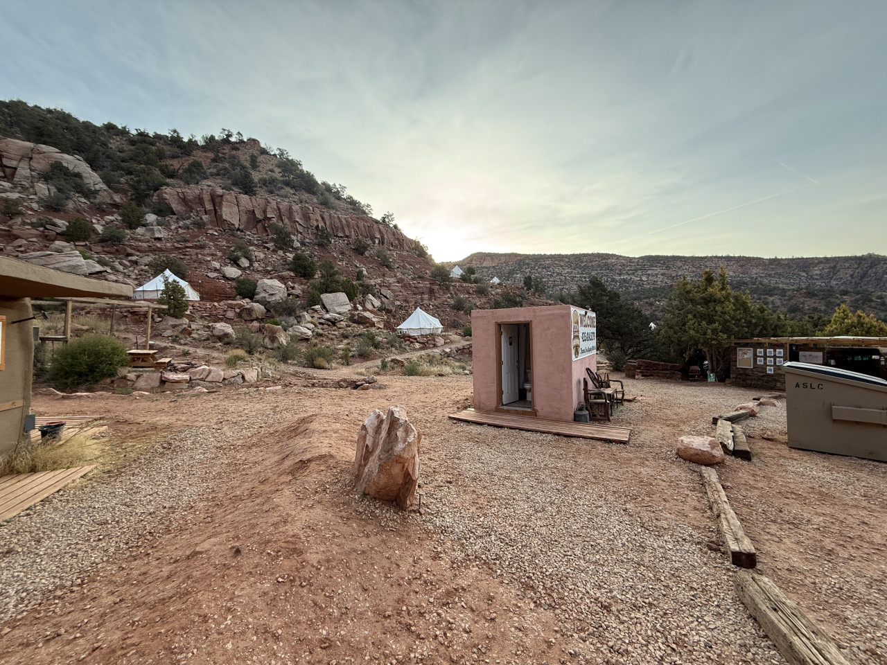 Glamping tábor v kaňonu, bílé stany na svahu, budka a nápis ASLC.
