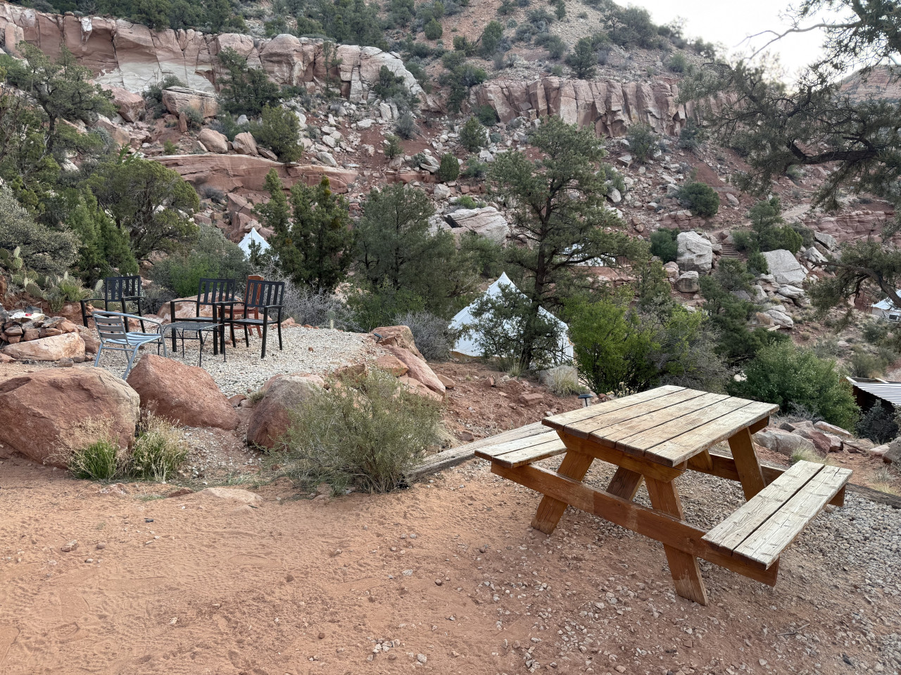 Dřevěný piknikový stůl a židle u ohniště, v pozadí bílé glamping stany