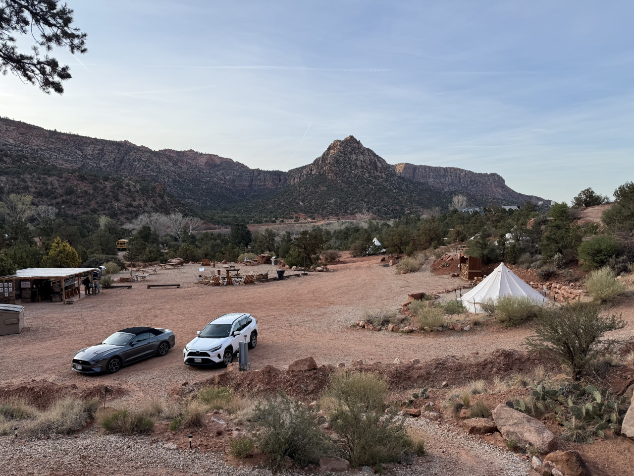 Glamping tábor u Zionu: bílé teepee, dvě auta a hory v pozadí.