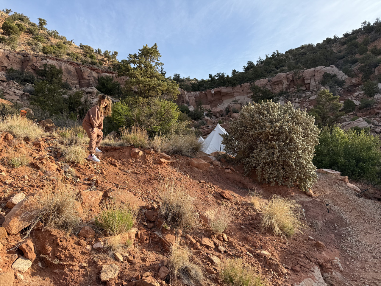Žena na červeném svahu nad bílými glampingovými stany v kaňonu.
