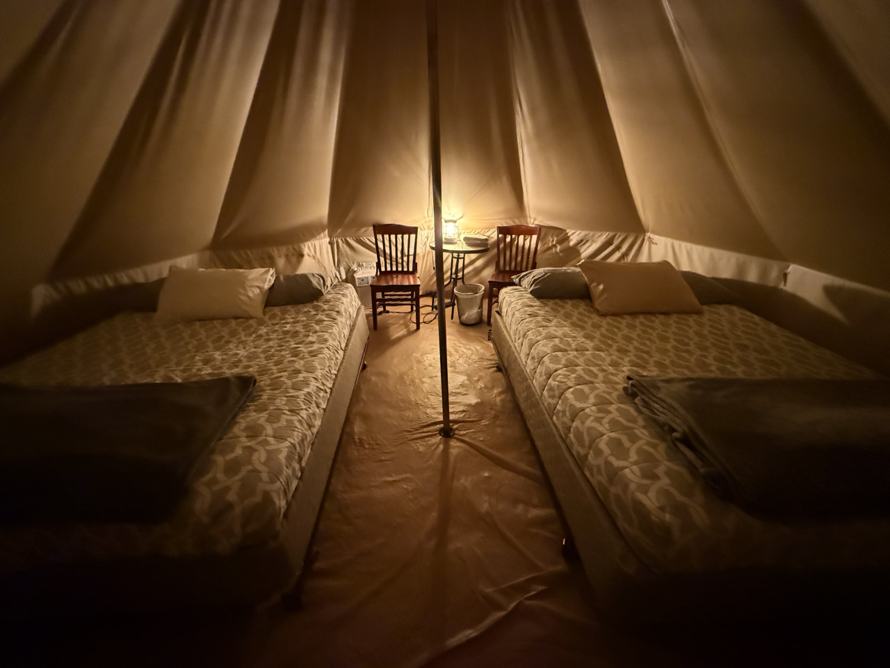 Interiér glampingového stanu se dvěma postelemi, lampou, dvěma židlemi a stolkem