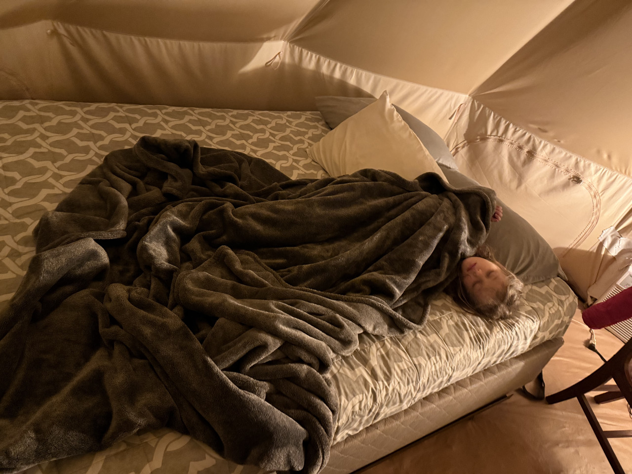 Osoba spí pod dekou na velké posteli uvnitř glampingového stanu