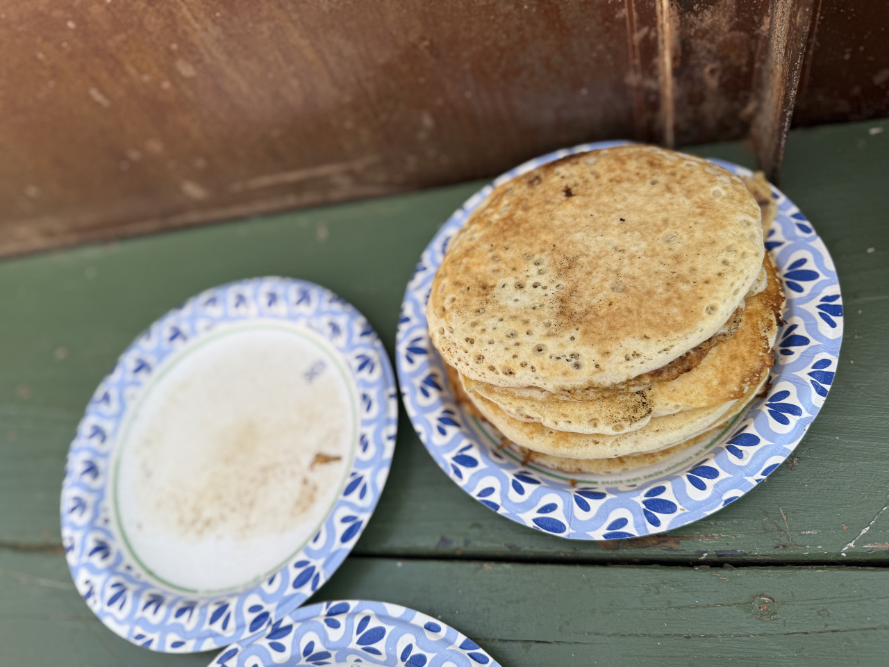 Hromádka palačinek na papírovém talíři, vedle prázdný špinavý talíř na lavici