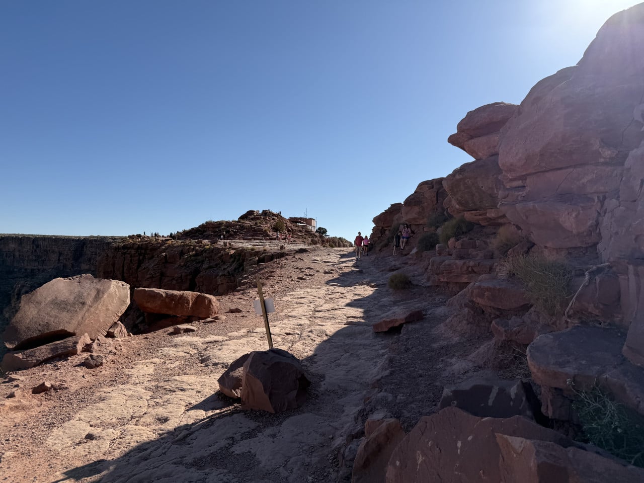 Kamenitá stezka u okraje kaňonu, turisté a modrá obloha.