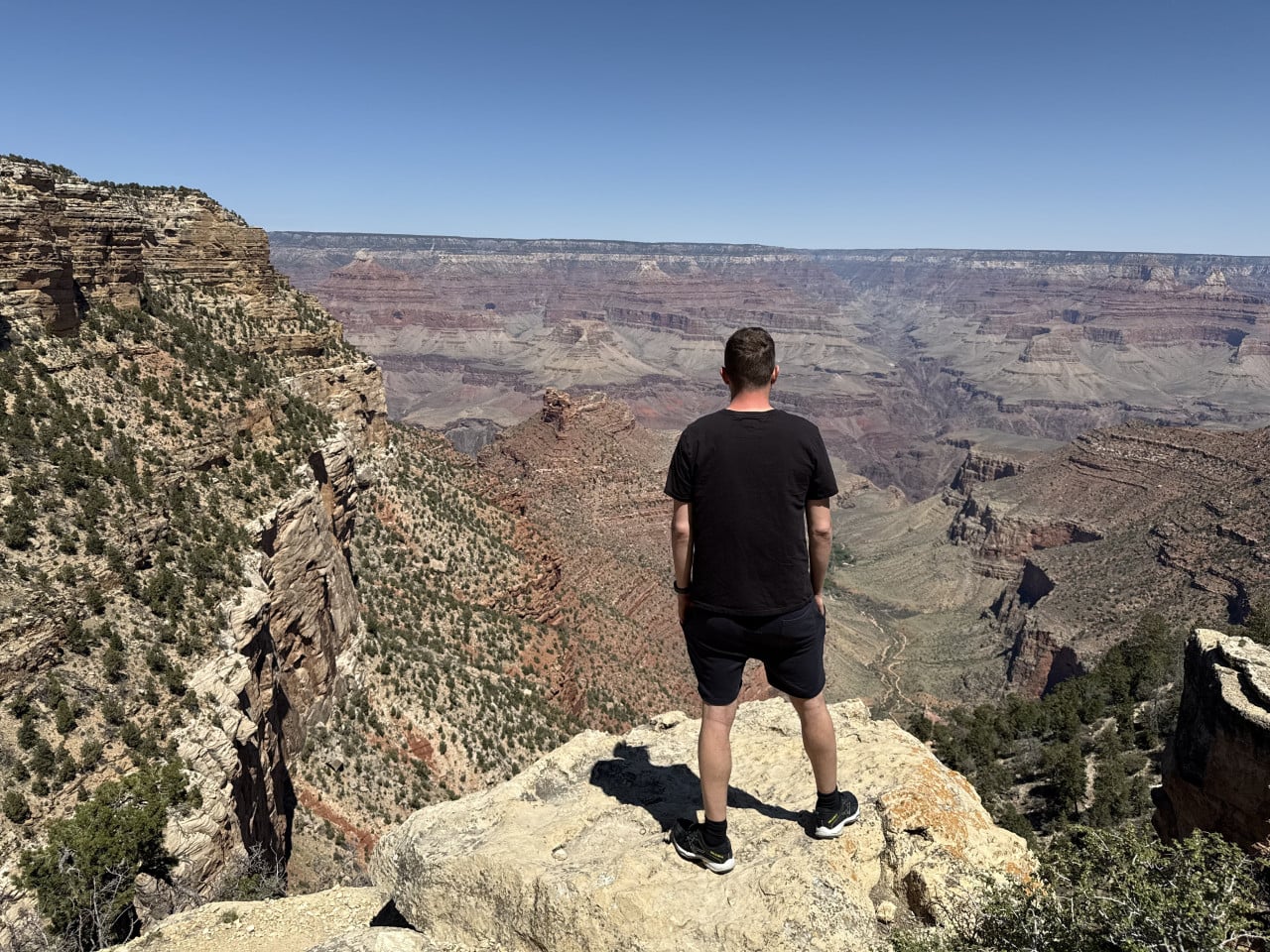 Muž stojí na vyhlídce nad Grand Canyonem, dívá se do kaňonu.