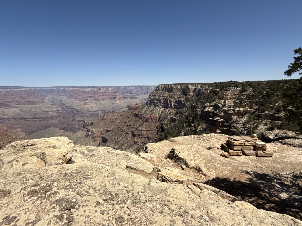 Výhled na Grand Canyon z kamenitého okraje pod modrou oblohou, bez lidí.