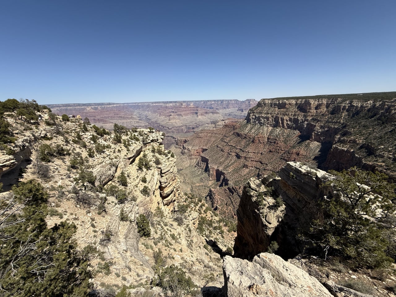 Panoramatický výhled na Grand Canyon z kamenitého trailu, modrá obloha.
