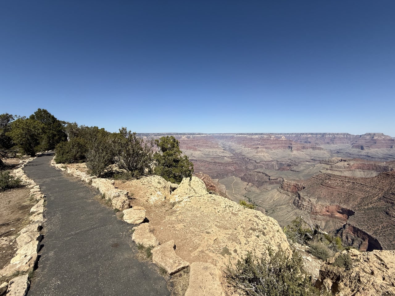 Stezka podél okraje Grand Canyonu s výhledem do kaňonu a modrou oblohou