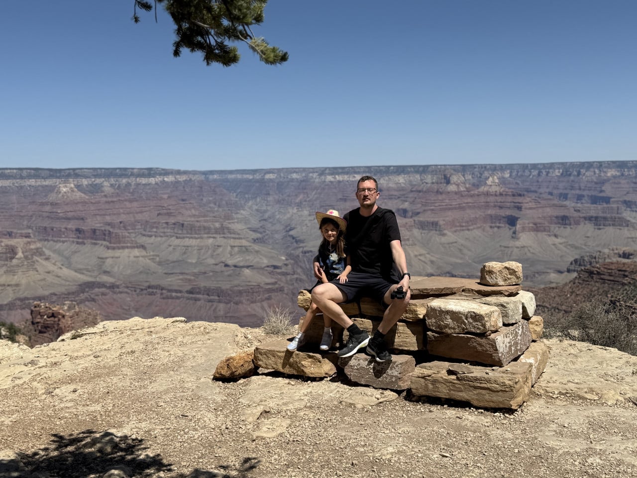 Muž a dítě sedí na kamenné lavičce s výhledem na Grand Canyon