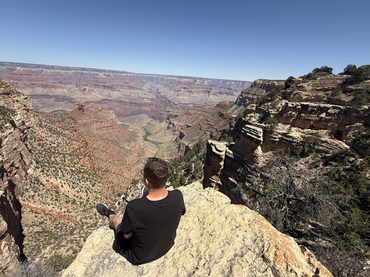 Muž sedí na skalním útesu nad Grand Canyonem a hledí do údolí.