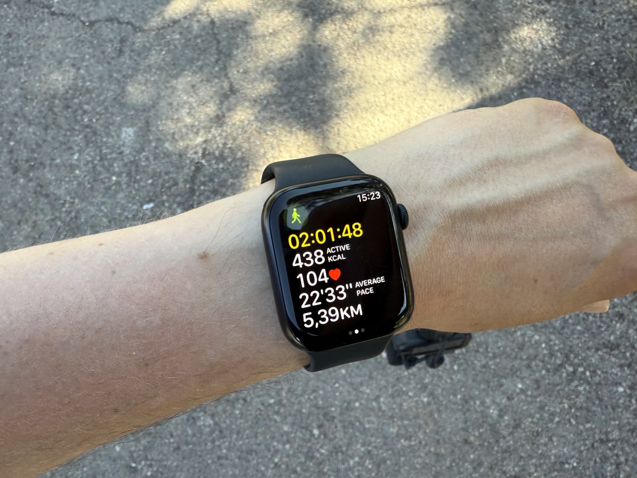 Zápěstí s Apple Watch zobrazující údaje o túře na asfaltové cestě.