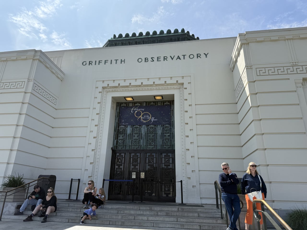 Pohled na vstupní fasádu Griffith Observatory v Los Angeles s návštěvníky na schodech.