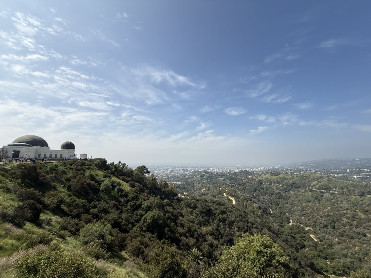 Griffith Observatory nad zelenými kopci s panoramatem Los Angeles pod modrou oblohou