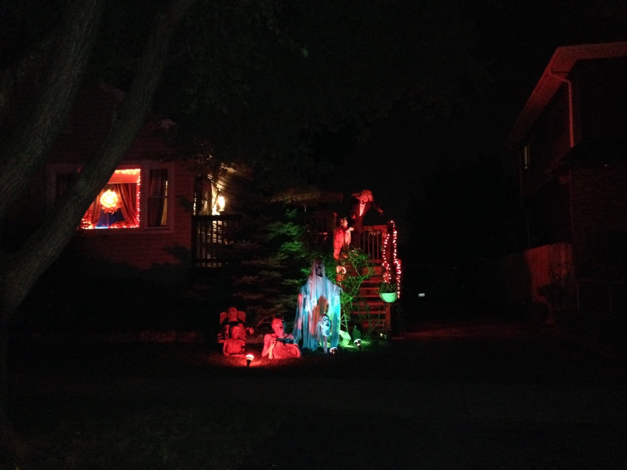 Noční dům s halloweenskou výzdobou, strašidla a červeně osvětlený vchod.