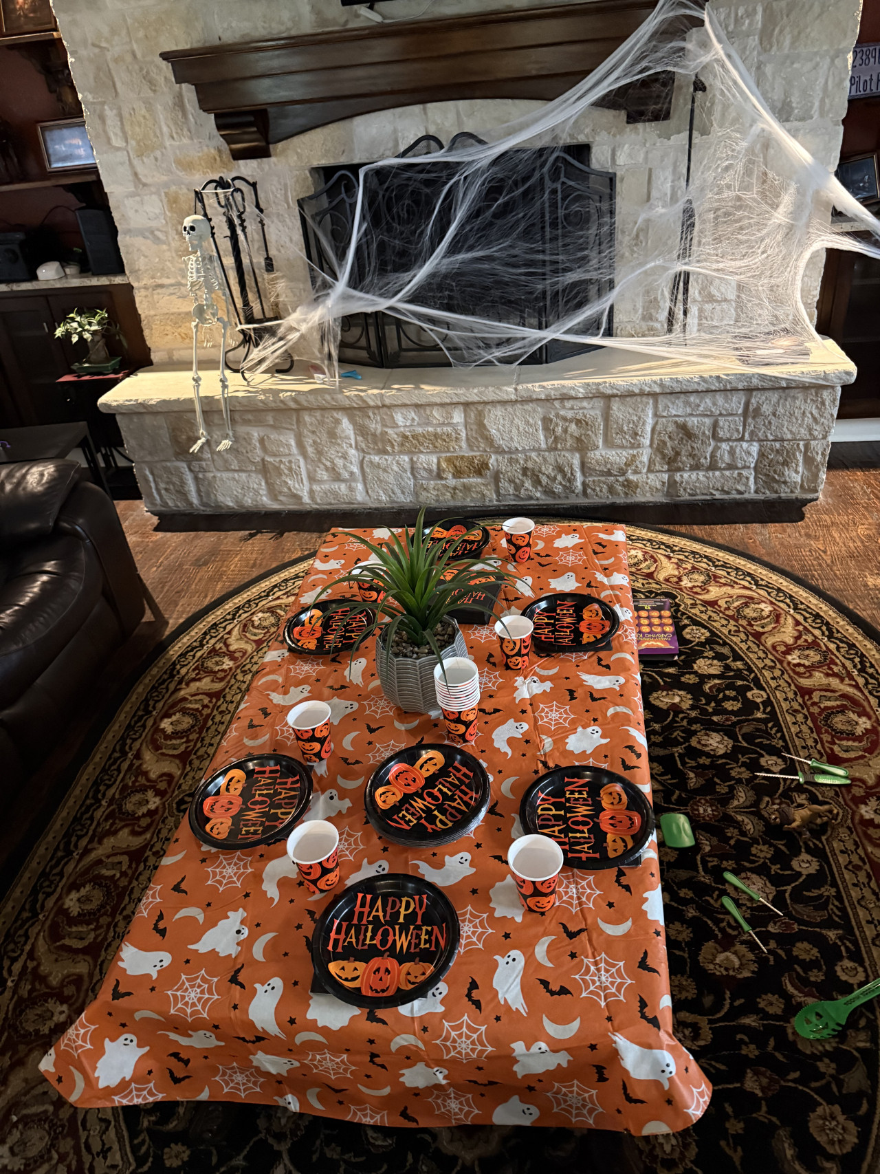 Halloweenově vyzdobený obývák s pavučinami, kostlivcem a stolem s talíři Happy Halloween.
