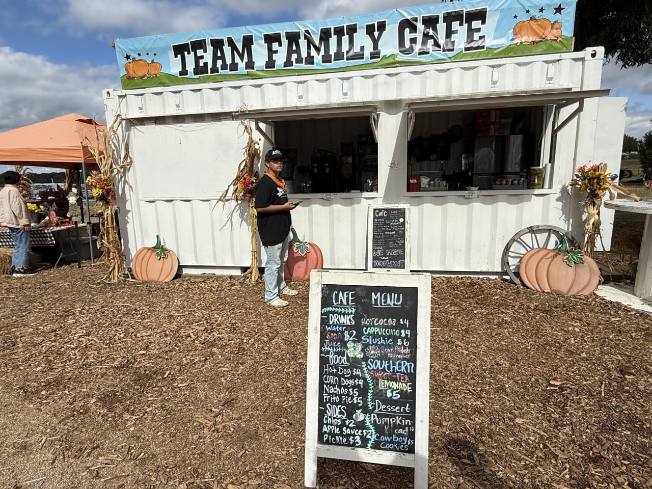 Podzimně vyzdobený stánek Team Family Cafe s menu tabulí a dýněmi na pumpkin patchi.