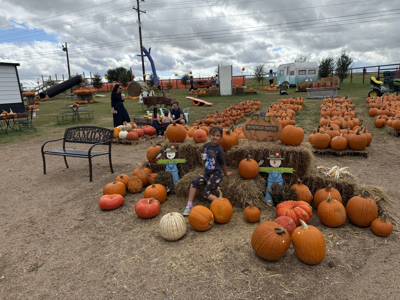 Pumpkin patch s dýněmi, rodinami a dětským posezením na balících slámy.