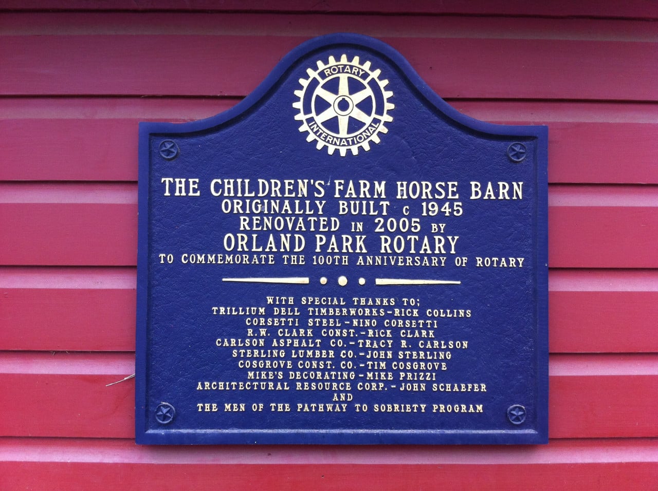Modrá pamětní tabule Rotary na červené dřevěné stěně s nápisem The Children’s Farm Horse Barn.