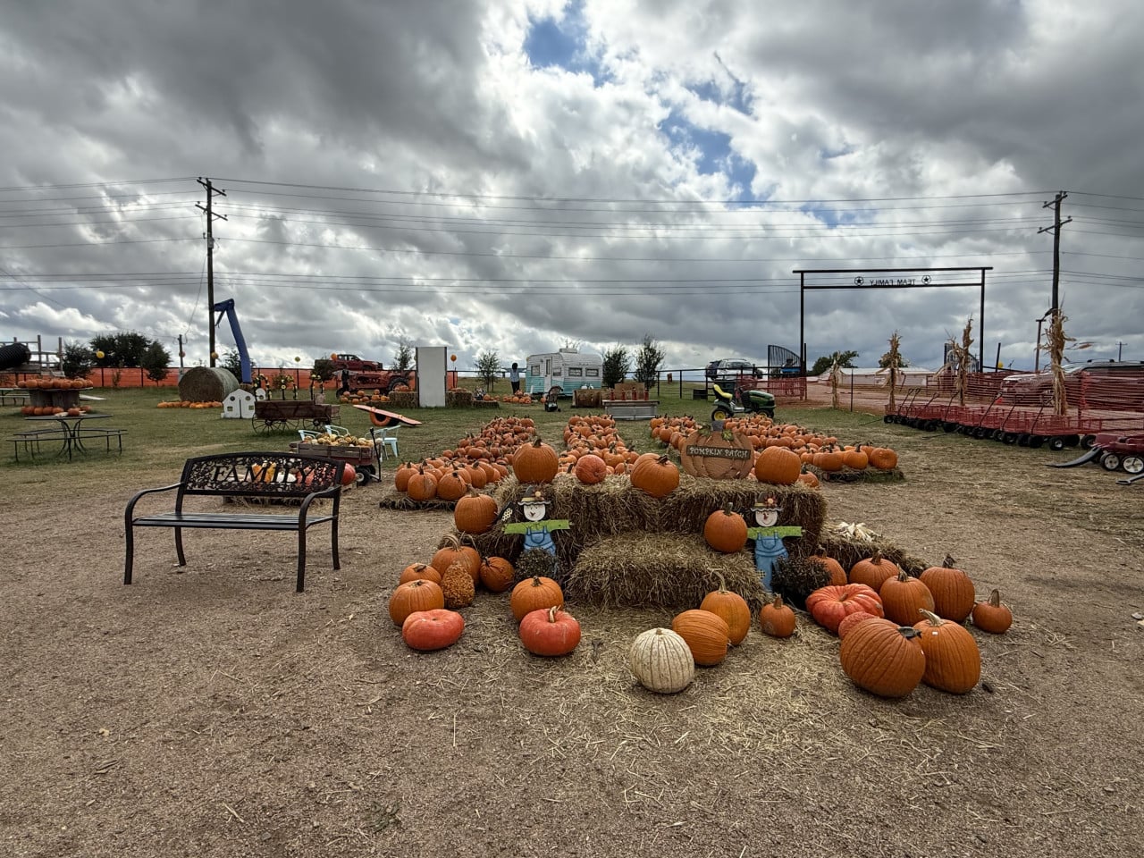 Dýňové pole s balíky slámy, nápisem pumpkin patch a podmračenou oblohou.