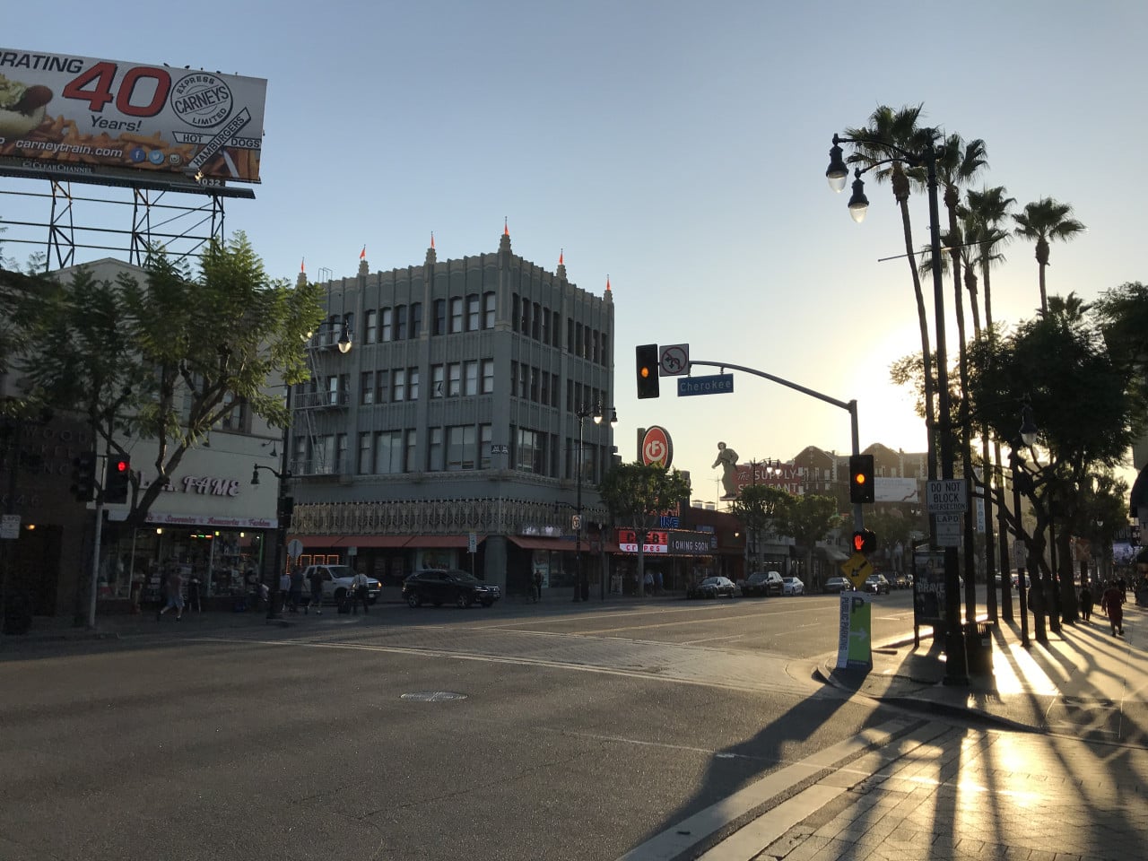 Hollywood Boulevard at sunset with palm trees, traffic lights, and a Carney billboard in Hollywood.