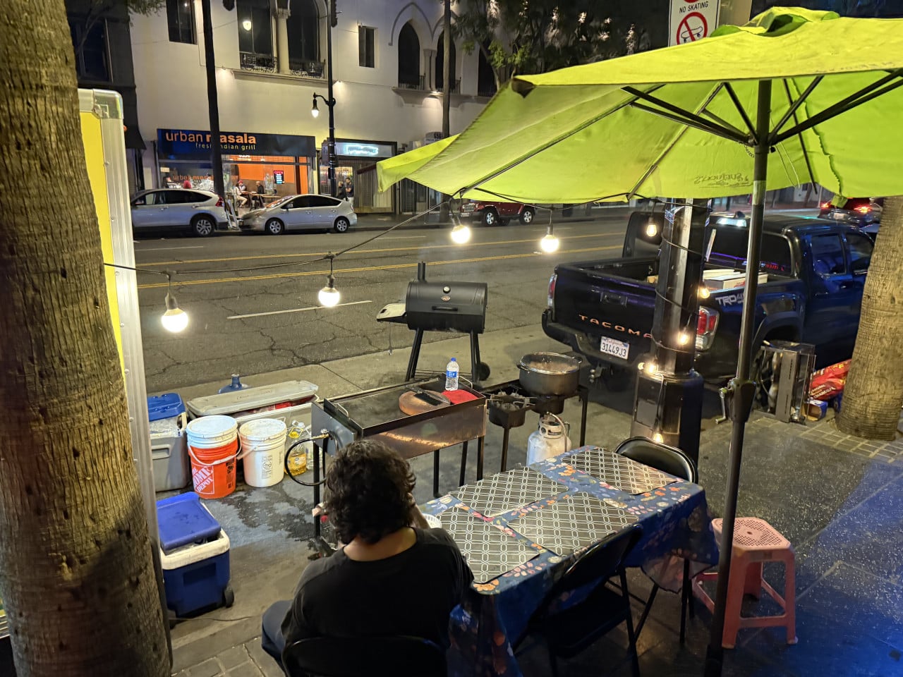 Noční pouliční stánek s grilem, zeleným slunečníkem a světly u chodníku v Hollywoodu