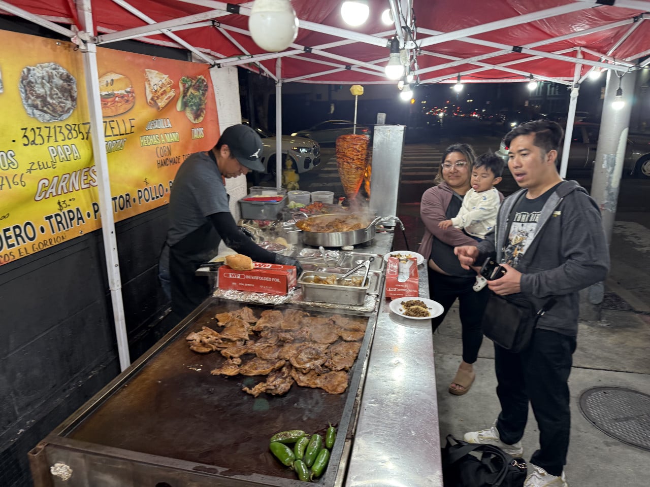 Pouliční stánek s grilem, prodavač servíruje maso rodině v noci.