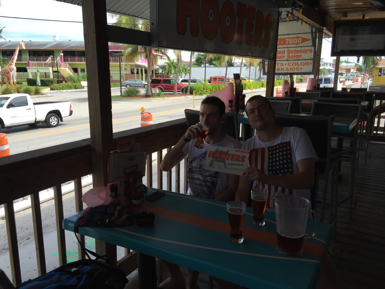 Dva muži na terase Hooters pijí pivo a drží menu HOOTERS of South Florida.