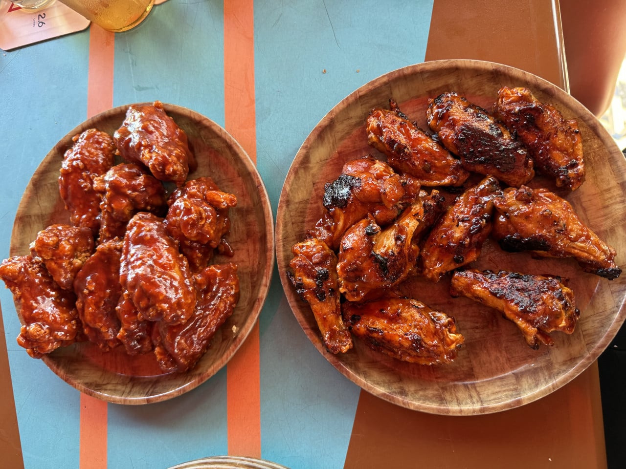 Dvě dřevěné mísy s kuřecími křidélky, jedna omáčka, druhá grilovaná.