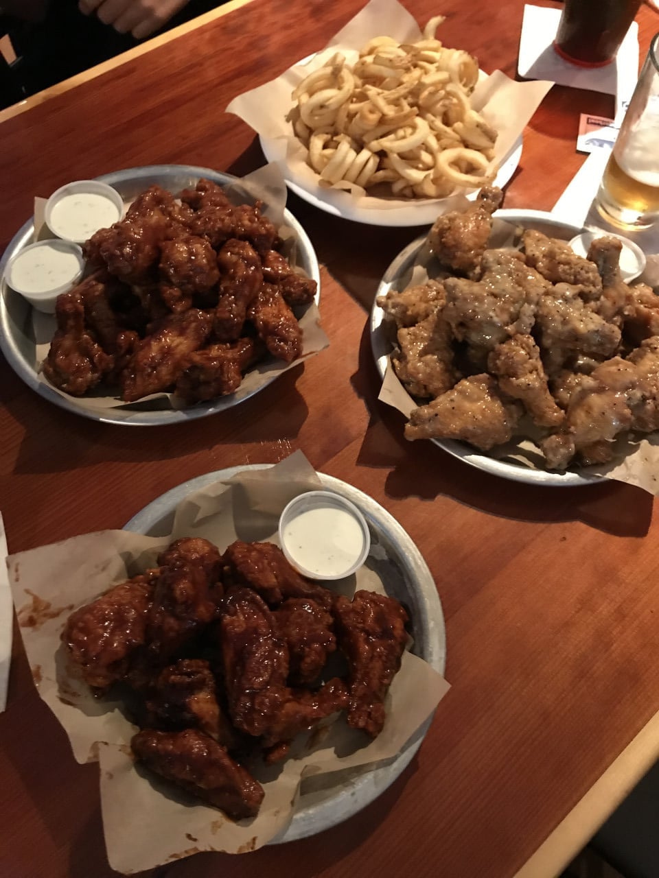 Tři talíře kuřecích křidélek s dipem a košík cibulových kroužků na stole