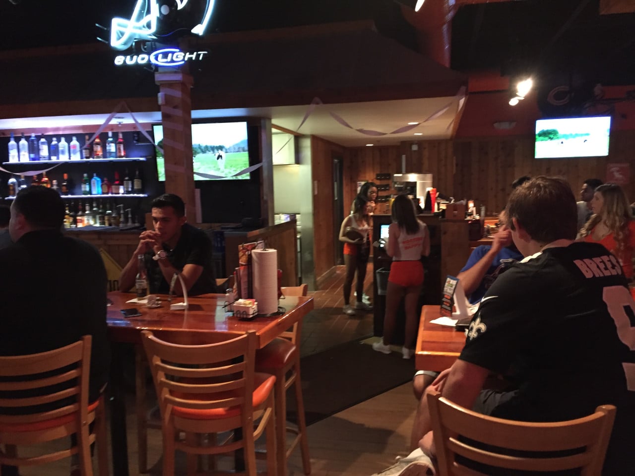 Interiér Hooters s hosty u stolů, servírkami, neonem BUD LIGHT, dres BREES