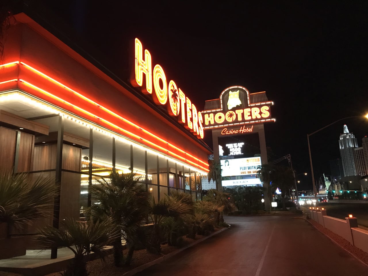 Noční fasáda Hooters s neonem HOOTERS, nápis Casino Hotel a billboard PLAY WITH US.