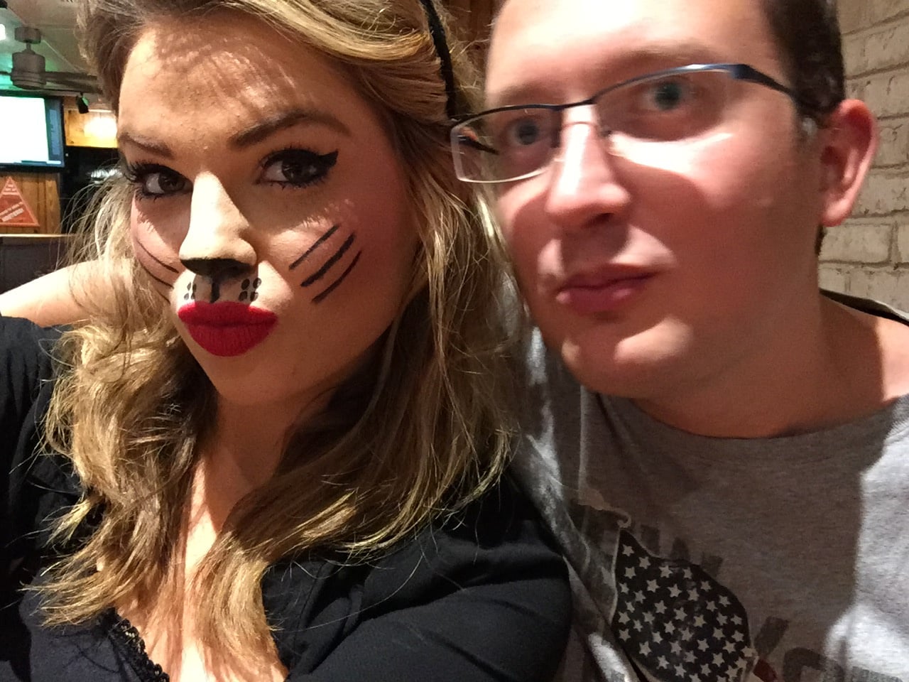 Selfie muže v brýlích a ženy s kočičím líčením a červenou rtěnkou.