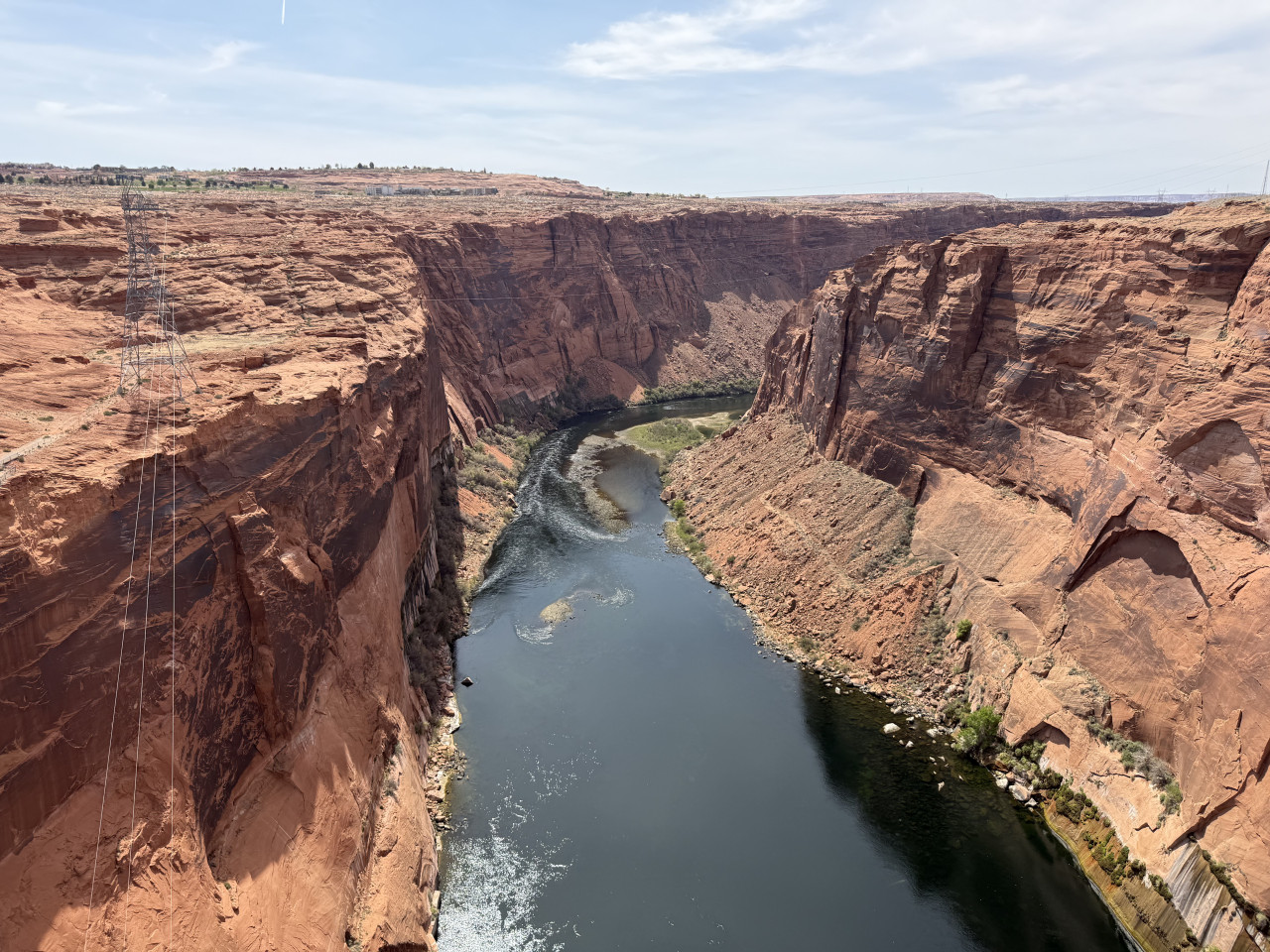 Řeka Colorado meandruje mezi červenými skalami kaňonu, vidět vedení vysokého napětí.