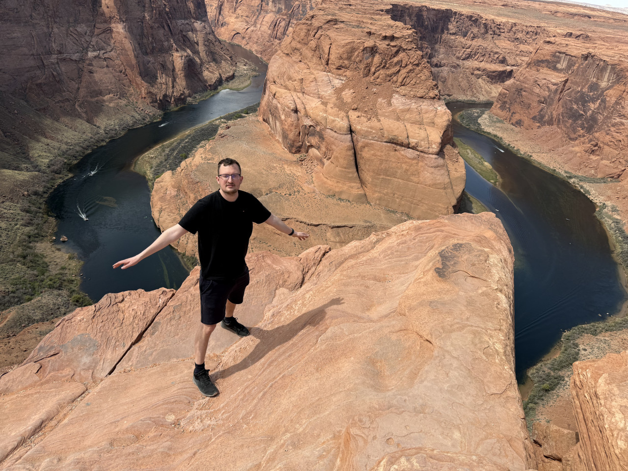 Muž na okraji skály nad Horseshoe Bend, meandr řeky Colorado.