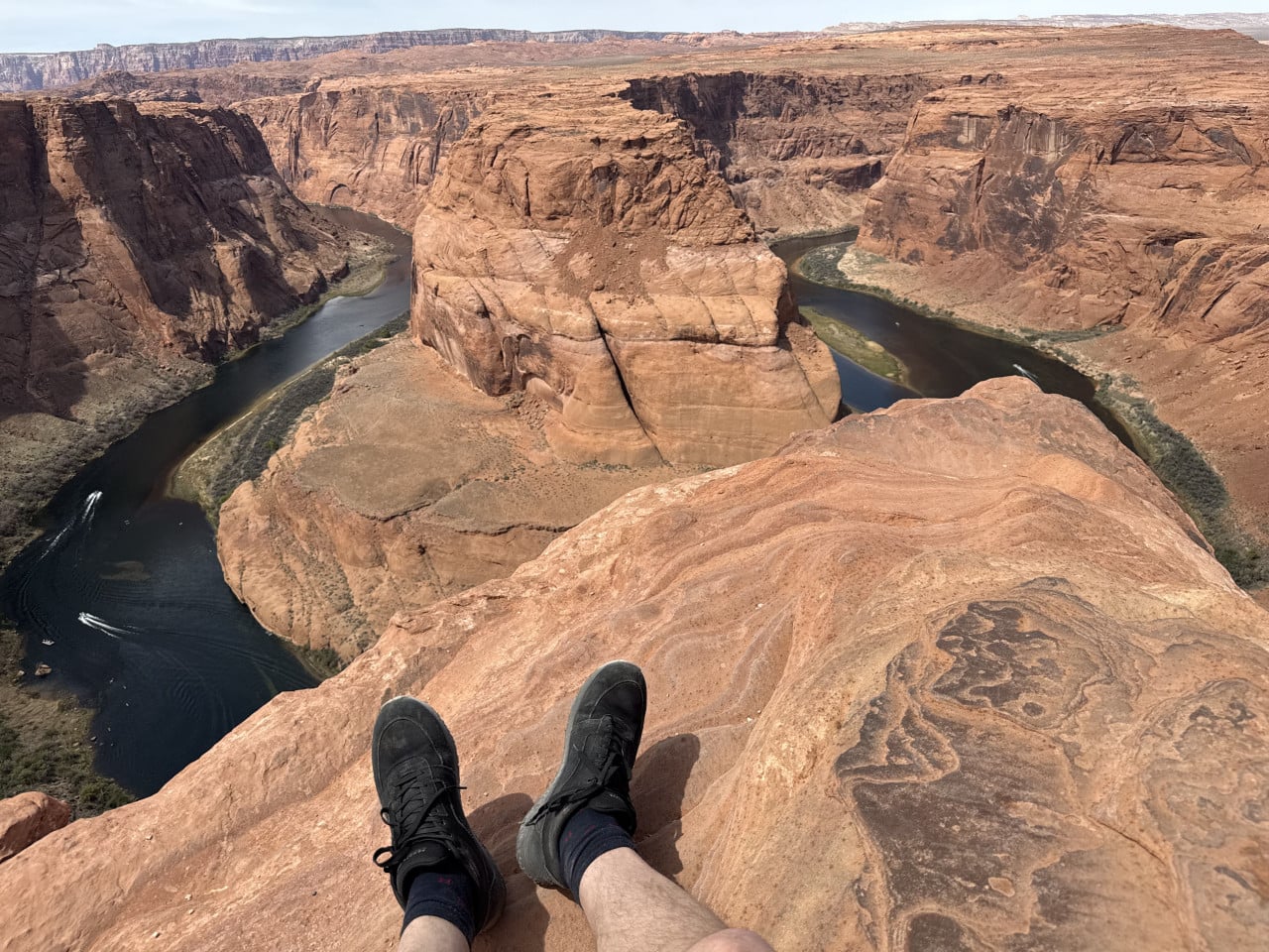 Pohled z útesu na Horseshoe Bend, řeka Colorado, v popředí nohy