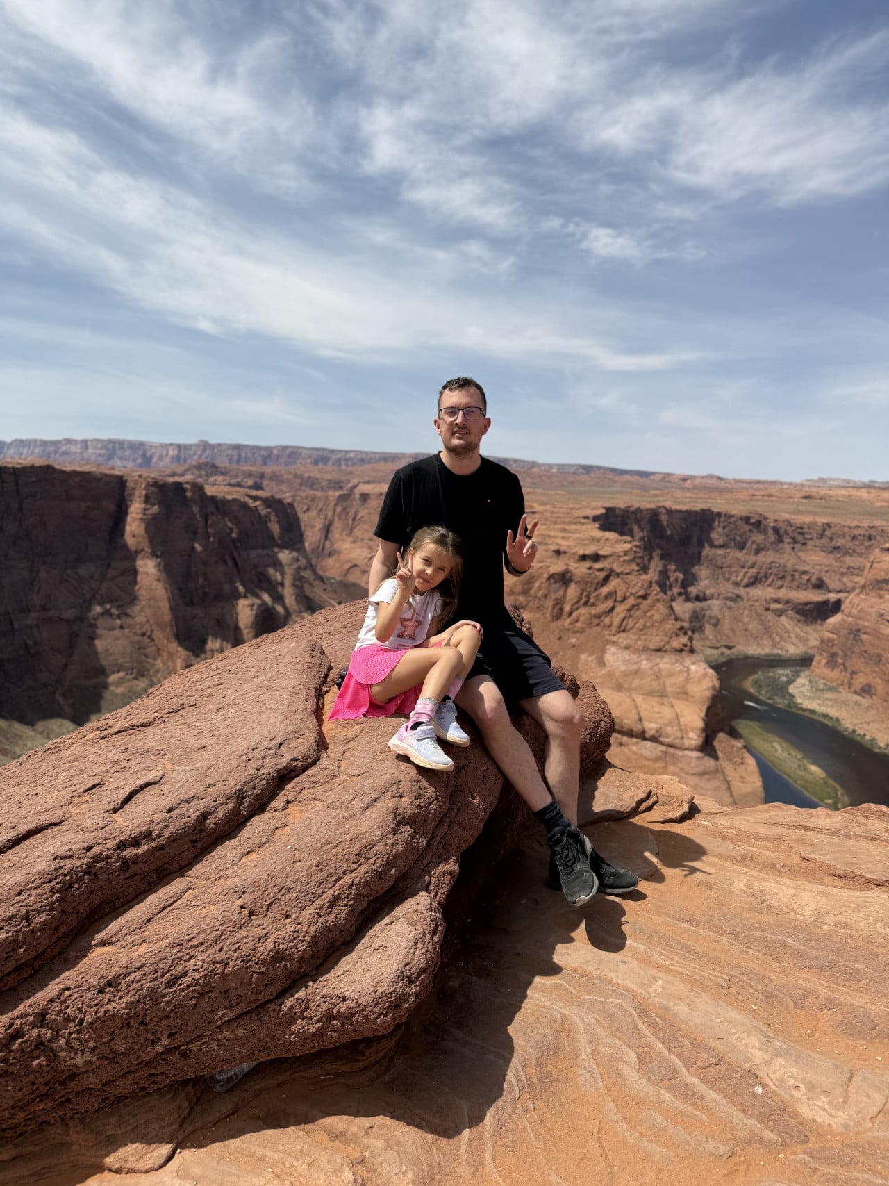 Muž s dívkou sedí na skále nad kaňonem Horseshoe Bend a řekou Colorado