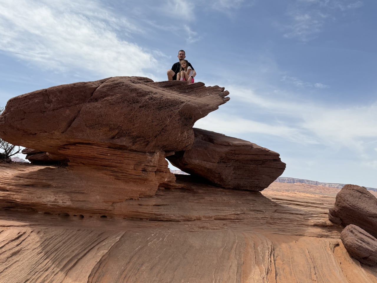Muž a dítě sedí na vrcholu červené pískovcové skály v poušti.